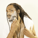 An organic man with dreadlocks brushing his beard, showcasing his commitment to no chemicals and quality mens care using the Shave Puck from Mountaineer Brand Products.