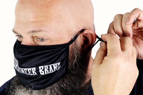 A man with a beard is applying a Mountaineer Brand Reusable Cloth Face Mask.