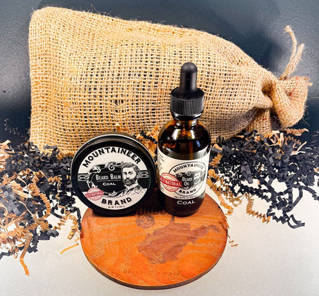 A bottle of Mountaineer Brand beard oil and a sack containing a Limited Edition Revival WV Coal Beard Kit on a wooden board.