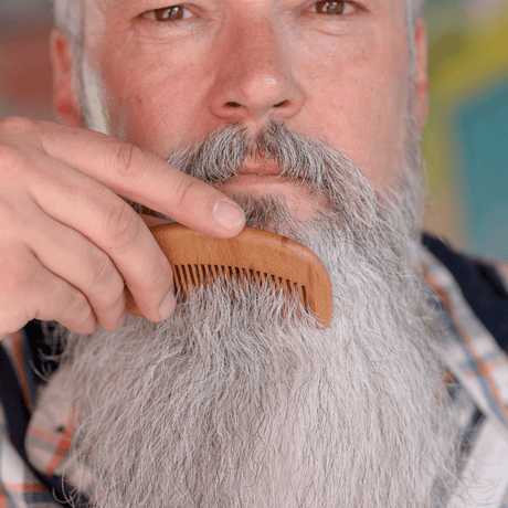 A man is grooming his beard with a Mountaineer Brand Products Wooden Beard Comb.