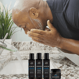 A man meticulously shaves in front of a sink, utilizing four carefully selected Mountaineer Brand Products from The Essential Bald Head Care System that contain natural ingredients, ensuring a sleek and non-greasy look.