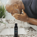 A man uses Mountaineer Brand Products' Bald Head Cleanse to shave his beard in front of a sink.