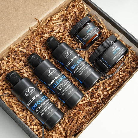 A set of Mountaineer Brand Products' The Complete Bald Head Care System, with natural ingredients, displayed in a gift box with wood shavings.