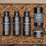 Four Mountaineer Brand Products for bald head care, including exfoliate, cleanse, balance, and deodorant with natural ingredients, arranged on a bed of straw.