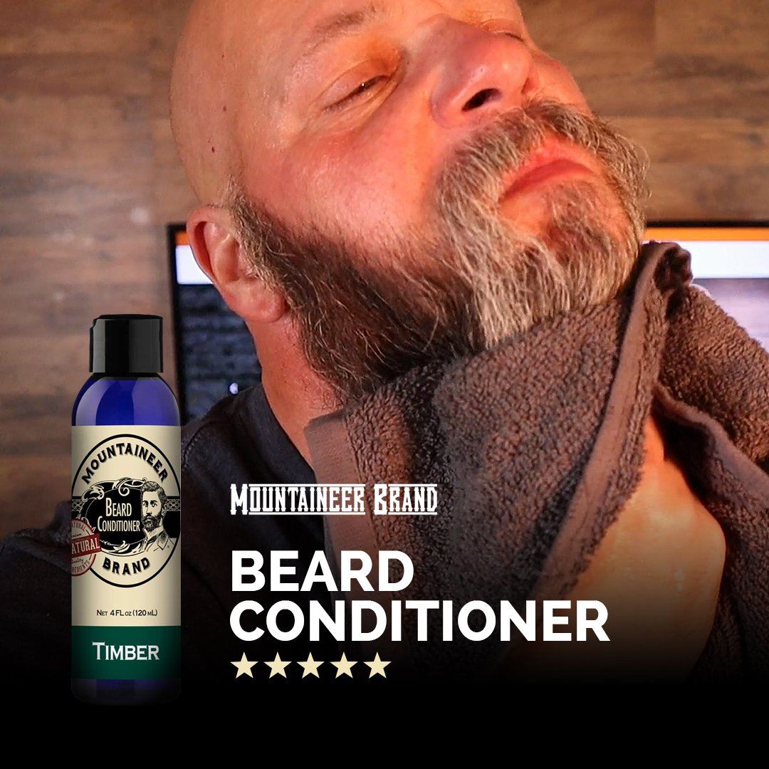 A bald man with a beard and closed eyes, feeling his soft beard, next to a bottle of Mountaineer Brand Products' Natural Beard Conditioner with five-star reviews.