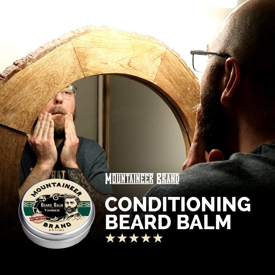 Man applying Mountaineer Brand Products' Natural Beard Balm, reflected in a circular mirror, with product prominently displayed.