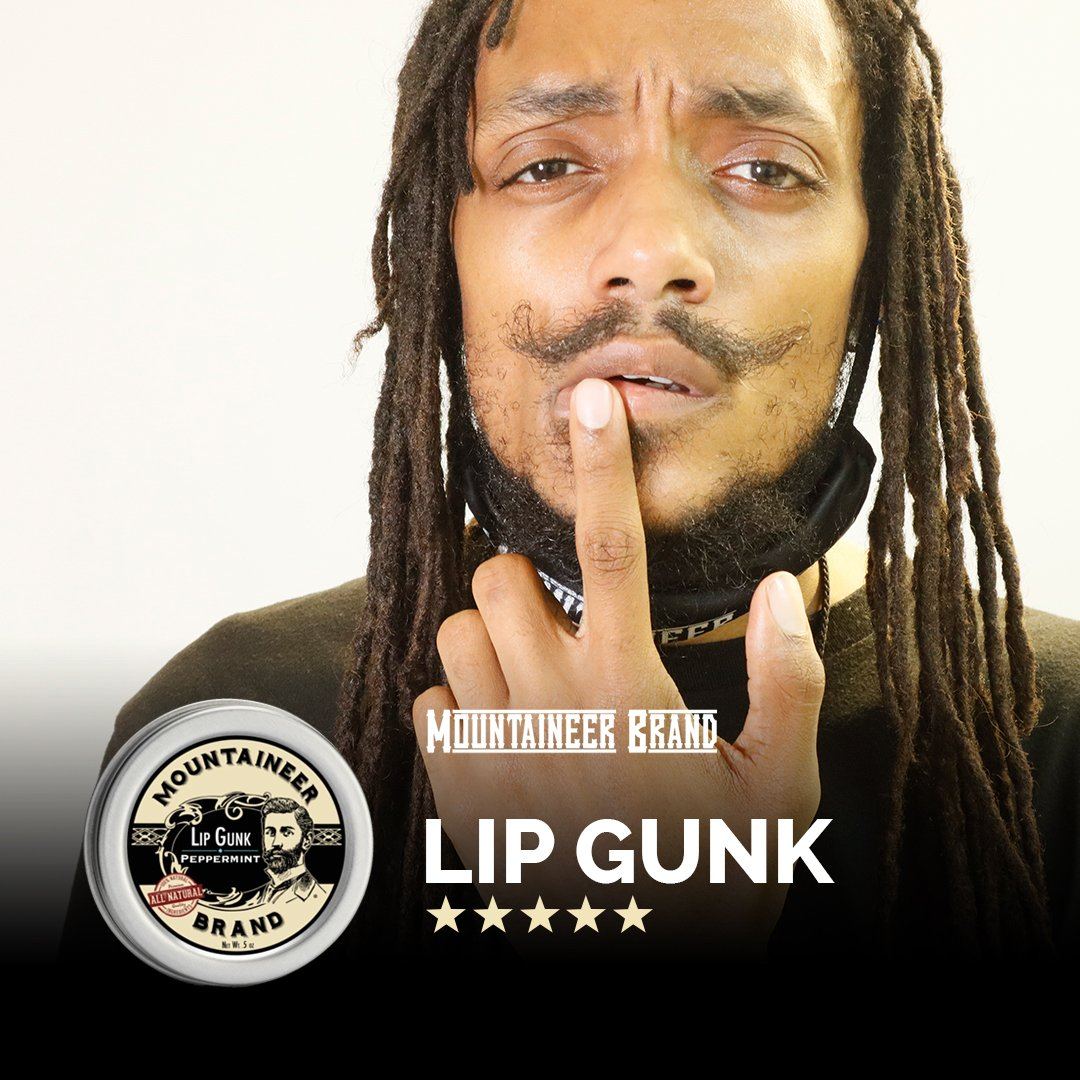 A man with dreadlocks is holding an LIP GUNK lip balm.