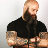 An all-natural man with a long beard and organic tattoos using Mountaineer Brand Products' Essential Bald Head Care System.