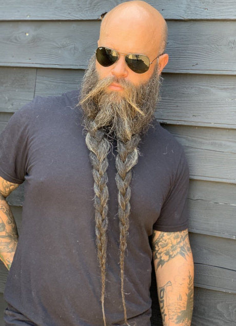 An all-natural bald man with a long beard and sunglasses, showcasing Mountaineer Brand Products' Conditioning Beard Balm (3 Pack) Mix & Match, an organic approach to men's care.